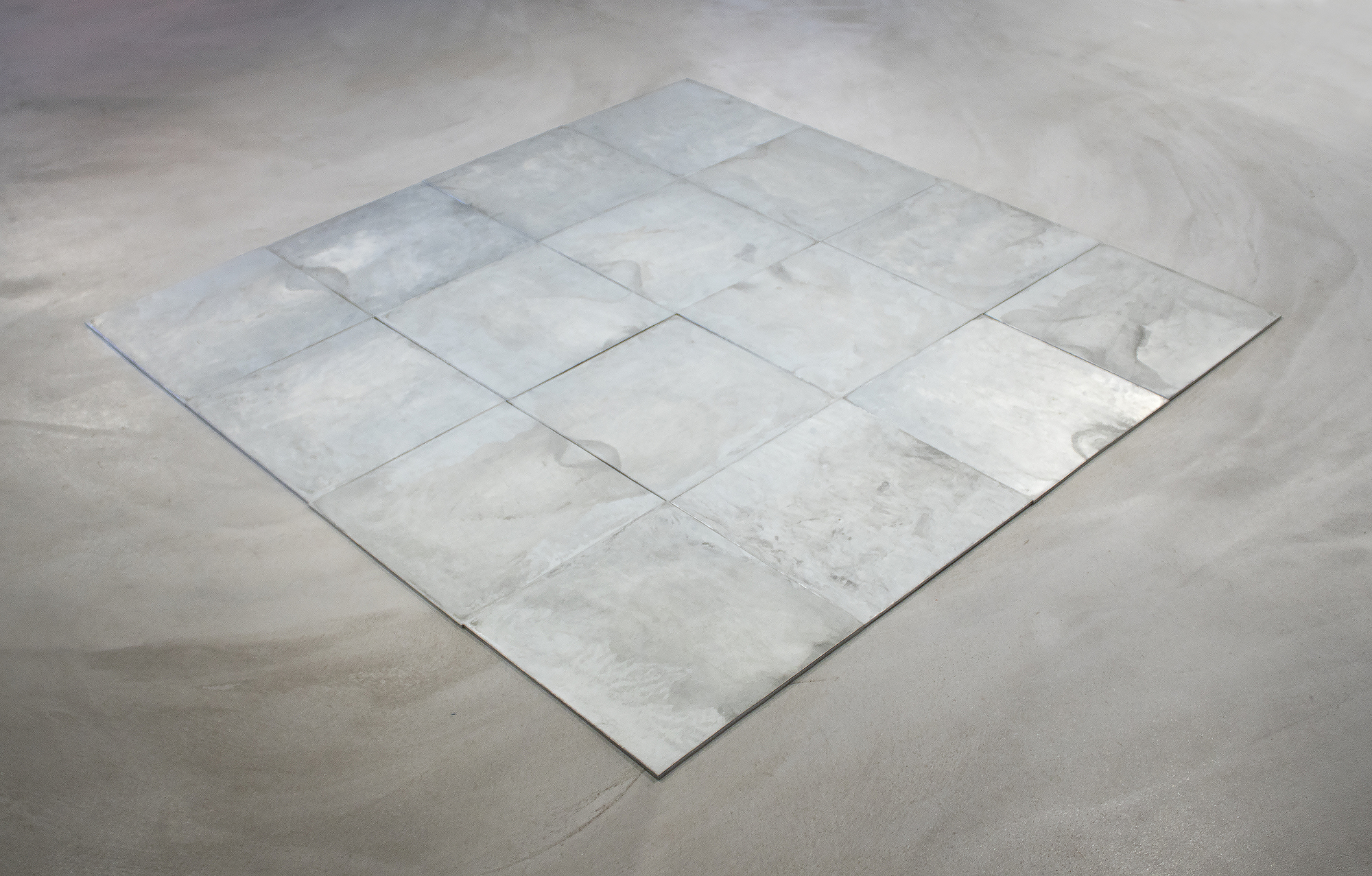CARL ANDRE - 16 Ace Zinc Square Carl Andre’s floor sculptures are typically made from glowing tiles of lead, zinc, or copper. They differ from most other minimalist artwork in their accessibility: they are meant to be walked on. Art historically, Andre places himself in the lineage of Constantin Brancusi and Henry Moore. Andre continues in their tradition of reducing the vocabulary of sculpture to its most vital and simple forms. The works also speak to Donald Judd’s idea of “specific objects,” which emphasized the phenomenological experience of the viewer and an exploration of structure and space.