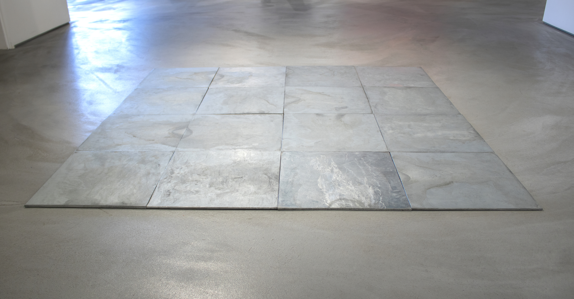 CARL ANDRE - 16 Ace Zinc Square Carl Andre’s floor sculptures are typically made from glowing tiles of lead, zinc, or copper. They differ from most other minimalist artwork in their accessibility: they are meant to be walked on. Art historically, Andre places himself in the lineage of Constantin Brancusi and Henry Moore. Andre continues in their tradition of reducing the vocabulary of sculpture to its most vital and simple forms. The works also speak to Donald Judd’s idea of “specific objects,” which emphasized the phenomenological experience of the viewer and an exploration of structure and space.