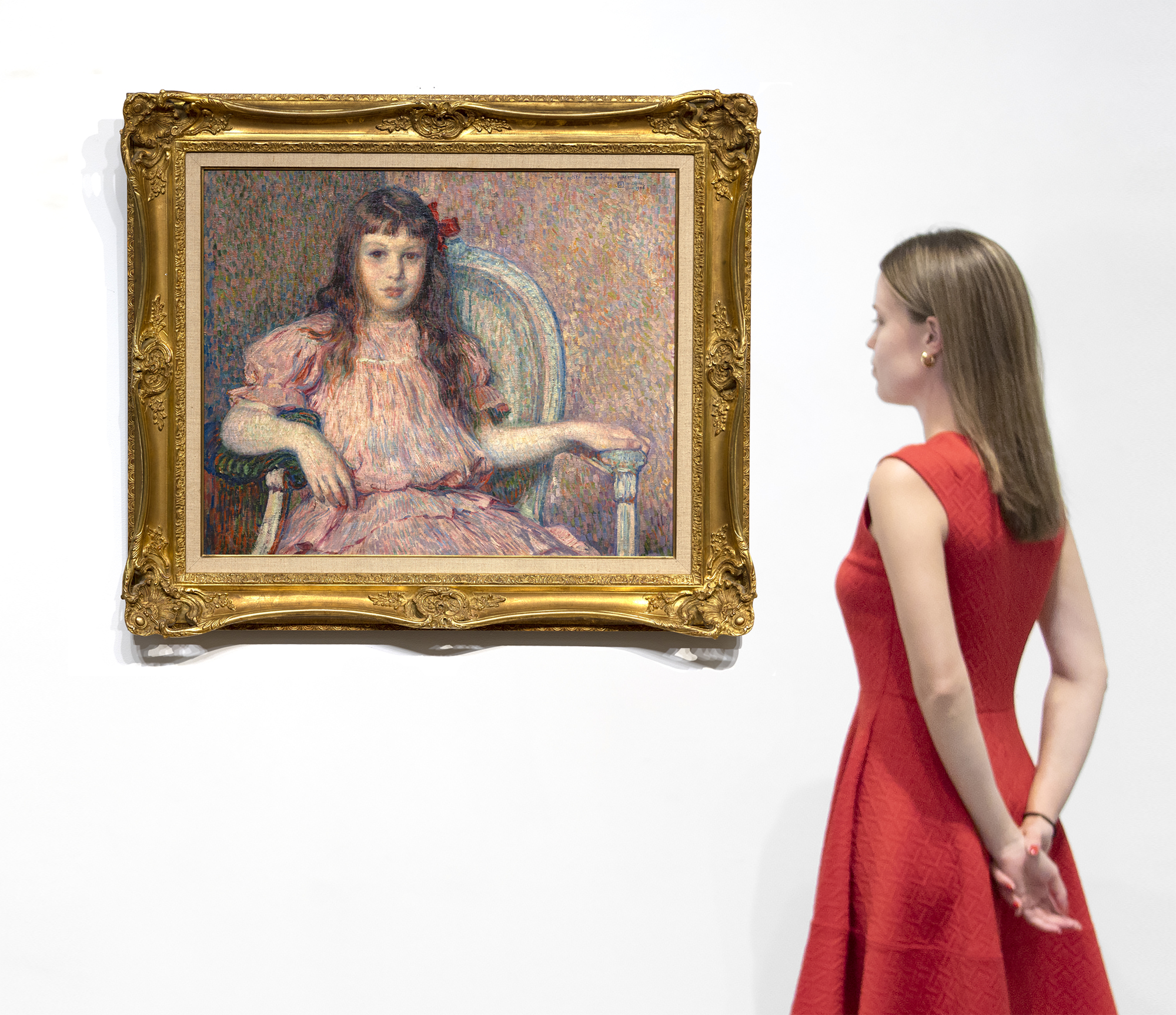 El Retrato de Sylvie Lacombe de Théo van Rysselberghe, pintado en 1906, es una obra maestra clásica de uno de los retratistas más refinados y coherentes de su época. El color es armonioso, la pincelada vigorosa y adaptada a su tarea material, su cuerpo y su semblante verdaderos y reveladores. La modelo es la hija de su buen amigo, el pintor Georges Lacombe, que compartió una estrecha asociación con Gauguin y fue miembro de Les Nabis con los artistas Bonnard, Denis y Vuillard, entre otros. Ahora conocemos a Sylvie Lacombe porque Van Rysselberghe es muy hábil en la representación de sutiles expresiones faciales y, a través de una cuidadosa observación y atención al detalle, nos ha proporcionado una visión de su mundo interior. Ha elegido una mirada directa, sus ojos a los tuyos, un pacto ineludible entre sujeto y espectador independientemente de nuestra relación física con el cuadro. Van Rysselberghe había abandonado en gran medida la técnica puntillista cuando pintó este retrato. Sin embargo, siguió aplicando las directrices de la teoría del color, utilizando tintes rojos -rosas y malvas- frente a verdes para crear una armoniosa paleta ameliorada de colores complementarios a la que añadió un fuerte acento para atraer la mirada: un lazo rojo intensamente saturado colocado asimétricamente a un lado de la cabeza.