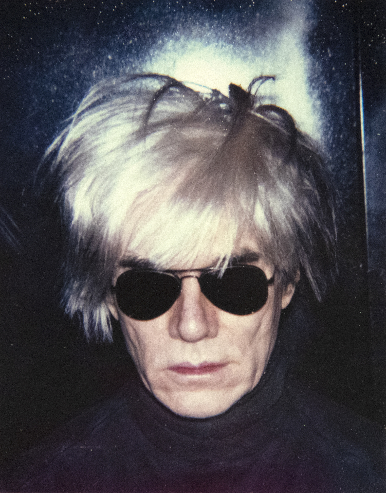 Beginning in 1963, with a silkscreen derived from a photo booth strip, Warhol repeatedly explored his likeness, culminating with the iconic "Fright Wig" image. Essential to his depiction of celebrities and self-representation, the Polaroid photograph played a crucial role in his work and our perceptions of his massive contribution to post-war art in America. The two images presented, dark and spooky, are beautifully crafted, well-staged portraits. Enveloped in a moody ambiance that eviscerates his body, these self-portraits depict Andy clad in this iconic wig and dark aviator sunglasses, set against a backdrop so deeply shadowed that his head seems to float in a void of darkness. Warhol loved role-playing, and here it is in spades!