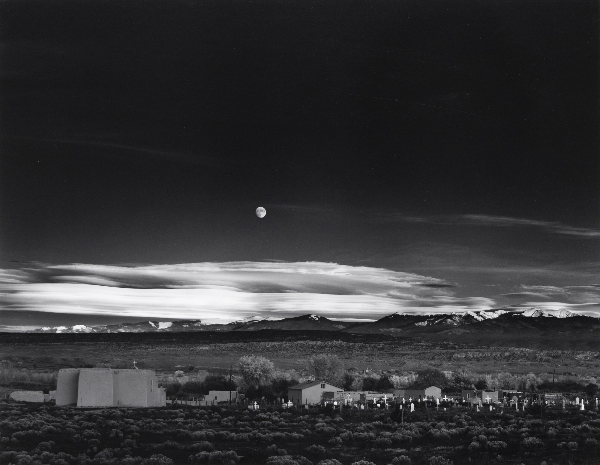 Known for his rigorous engagement in the darkroom, Ansel Adams created 1,300 prints of Moonrise, Hernandez over 40 years of dodging and burning, creating a longitudinal group of masterworks. Moonrise is a formidable composition that holds us in suspended appreciation for its hauntingly beautiful impression. We do not need to know of Ansel's desperate scramble to set his tripod, find his meter to grasp that transience, or ponder the kismet of capturing that moment. In this 1959 print, all the glorious details are present: the almost, but not quite, full moon with its discernable features and the essential graveyard with its glowing markers and starkly illuminated white crosses caught in the waning moment of daylight's inevitable retreat.