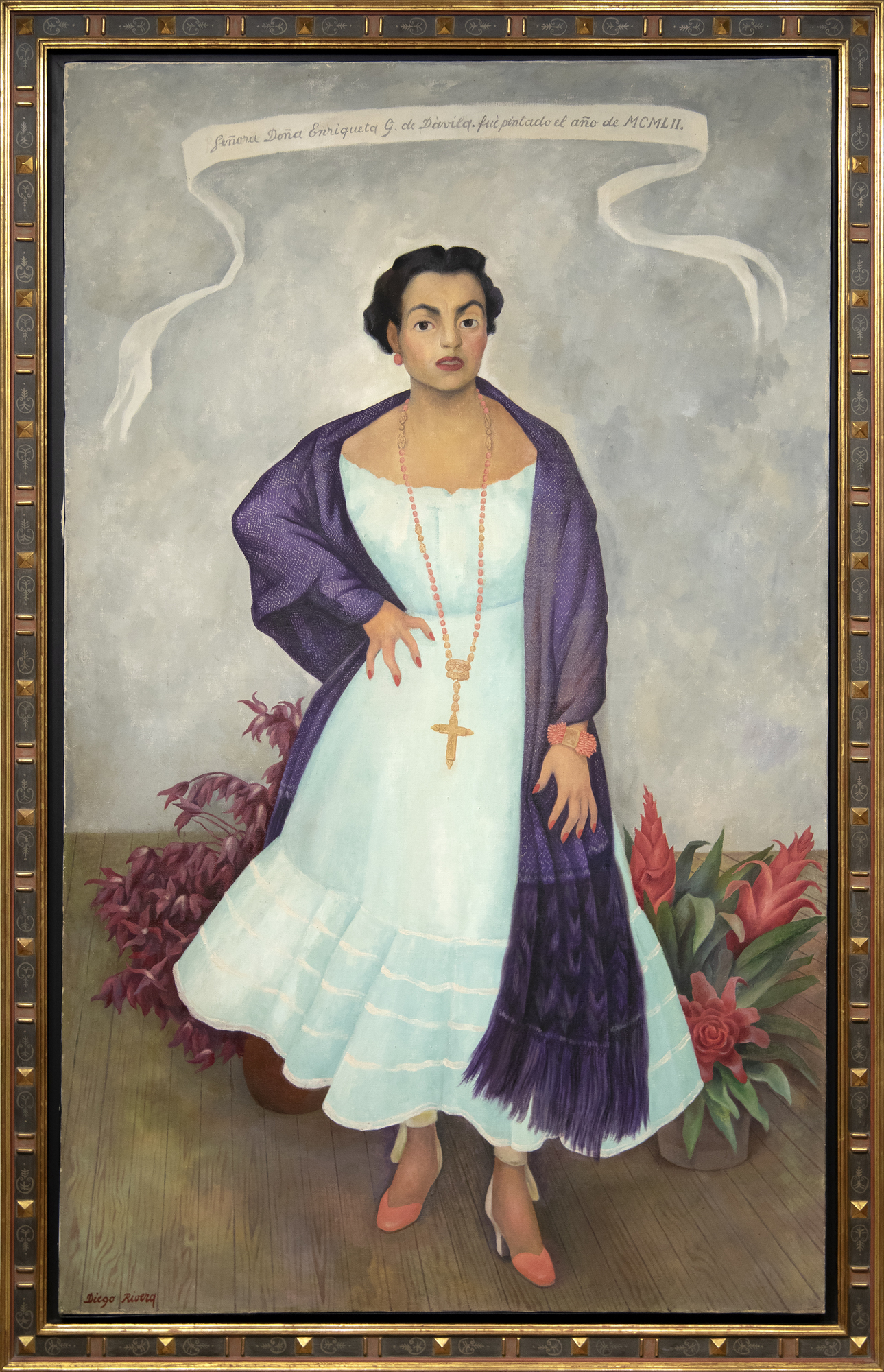 
<br>In Diego Rivera’s portrait of Enriqueta Dávila, the artist asserts a Mexicanidad, a quality of Mexican-ness, in the work along with his strong feelings towards the sitter. Moreover, this painting is unique amongst his portraiture in its use of symbolism, giving us a strong if opaque picture of the relationship between artist and sitter.
<br>
<br>Enriqueta, a descendent of the prominent Goldbaum family, was married to the theater entrepreneur, José María Dávila. The two were close friends with Rivera, and the artist initially requested to paint Enriqueta’s portrait. Enriqueta found the request unconventional and relented on the condition that Rivera paints her daughter, Enriqueta “Quetita”. Rivera captures the spirit of the mother through the use of duality in different sections of the painting, from the floorboards to her hands, and even the flowers. Why the split in the horizon of the floorboard? Why the prominent cross while Enriqueta’s family is Jewish? Even her pose is interesting, showcasing a woman in control of her own power, highlighted by her hand on her hip which Rivera referred to as a claw, further complicating our understanding of her stature.
<br>
<br>This use of flowers, along with her “rebozo” or shawl, asserts a Mexican identity. Rivera was adept at including and centering flowers in his works which became a kind of signature device. The flowers show bromeliads and roselles; the former is epiphytic and the latter known as flor de jamaica and often used in hibiscus tea and aguas frescas. There is a tension then between these two flowers, emphasizing the complicated relationship between Enriqueta and Rivera. On the one hand, Rivera demonstrates both his and the sitter’s Mexican identity despite the foreign root of Enriqueta’s family but there may be more pointed meaning revealing Rivera’s feelings to the subject. The flowers, as they often do in still life paintings, may also refer to the fleeting nature of life and beauty. The portrait for her daughter shares some similarities from the use of shawl and flowers, but through simple changes in gestures and type and placement of flowers, Rivera illuminates a stronger personality in Enriqueta and a more dynamic relationship as filtered through his lens.
<br>
<br>A closer examination of even her clothing reveals profound meaning. Instead of a dress more in line for a socialite, Rivera has Enriqueta in a regional dress from Jalisco, emphasizing both of their Mexican identities. On the other hand, her coral jewelry, repeated in the color of her shoes, hints at multiple meanings from foreignness and exoticism to protection and vitality. From Ancient Egypt to Classical Rome to today, coral has been used for jewelry and to have been believed to have properties both real and symbolic. Coral jewelry is seen in Renaissance paintings indicating the vitality and purity of woman or as a protective amulet for infants. It is also used as a reminder, when paired with the infant Jesus, of his future sacrifice. Diego’s use of coral recalls these Renaissance portraits, supported by the plain background of the painting and the ribbon indicating the maker and date similar to Old Master works.
<br>
<br>When combined in the portrait of Enriqueta, we get a layered and tense building of symbolism. Rivera both emphasizes her Mexican identity but also her foreign roots. He symbolizes her beauty and vitality but look closely at half of her face and it is as if Rivera has painted his own features onto hers. The richness of symbolism hints at the complex relationship between artist and sitter.
