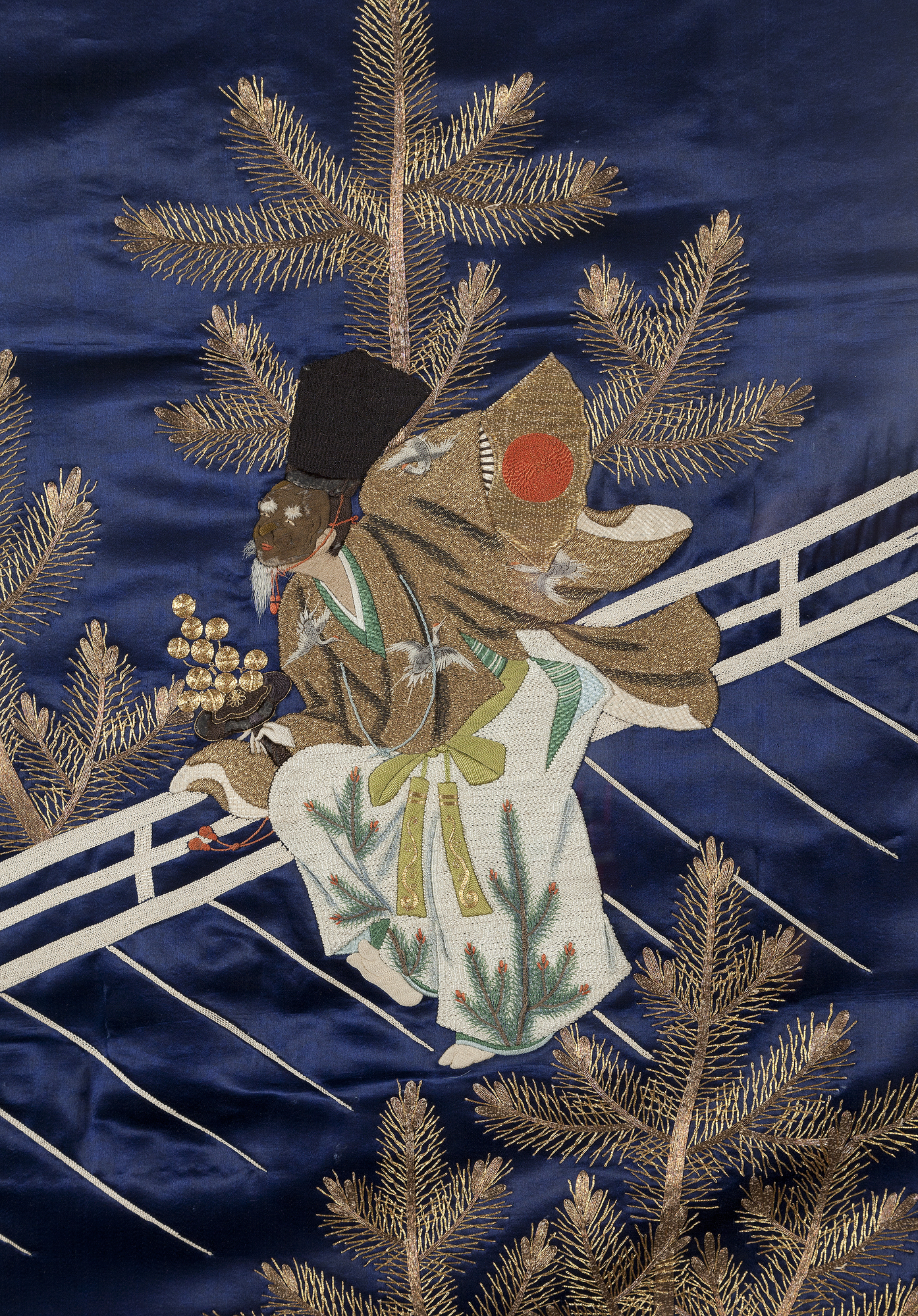 Here, a Noh actor in full costume and mask is crossing the wing of a Noh stage. The stage is flanked by pine trees, and pines are also a motif on his kimono. Typically a pine tree is painted on the back wall of Noh stages to represent the tree through which this theatrical form was, by legend, passed down from heaven to mankind. In Japanese culture, the evergreen pine has come to be an important symbol of longevity and steadfastness.<br><br>The practice of laying fukusa over presents placed on wooden or lacquer trays became wide spread during the Edo period, (17th to 19th century). What begun as a functional practice to protect gifts from the elements, took on a decorative life of its own. Well-to-do families owned large numbers of fukusa and often commissioned famous artists of the<br>time to design exclusively for them. The drawings were then created by such techniques as tie-dying, stenciling, slit embroidery, tapestry, painting with embroidery and combinations of all methods. Each time a fukusa was required, it was chosen not only for the occasion but also for the season, the gift itself, and the status of the donor and the recipient. Fukusa were also part of the brides’ trousseau and could be given on the occasion of a wedding. Fukusa were made of square or oblong pieces of silk, lined and often embellished with tassels, and sometimes bearing the monogram or family crest on the reverse. Etiquette decreed that the fukusa were not usually to be considered part of the gift itself and were to be returned covering a token gift or an acknowledgement of the gift. However, some recipients such as bureaucrats, who accepted gifts from people currying favors, elected to keep the fukusa along with the gifts they covered, thus adding to their own store of gift covers.