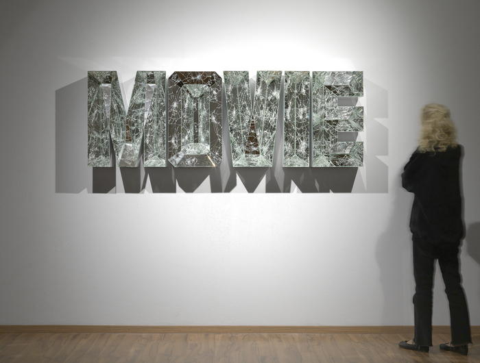 DOUG AITKEN - Movie Doug Aitken is best known as a video artist who experiments with radically expanded or fragmented screens. The mirror is a central motif in his sculptures, installations, and films. His 2011 film “Black Mirror,” starring Chloe Sevigny was commissioned by the collector Dakis Joannou and debuted on a floating barge off the coast of Greece. His groundbreaking underwater art installation off Catalina Island in 2016 involved pavilions with mirrored surfaces to create kaleidoscopic visual effects, refracting the light streaming through the water. The use of mirror in this sculpture “Movie” from 2012 evokes a similar sense of fractured perception and creates a striking prismatic lighting effect. It comes from a series of text sculptures of punchy words, including Fate, Free, Now, Riot, Sex, and Star.